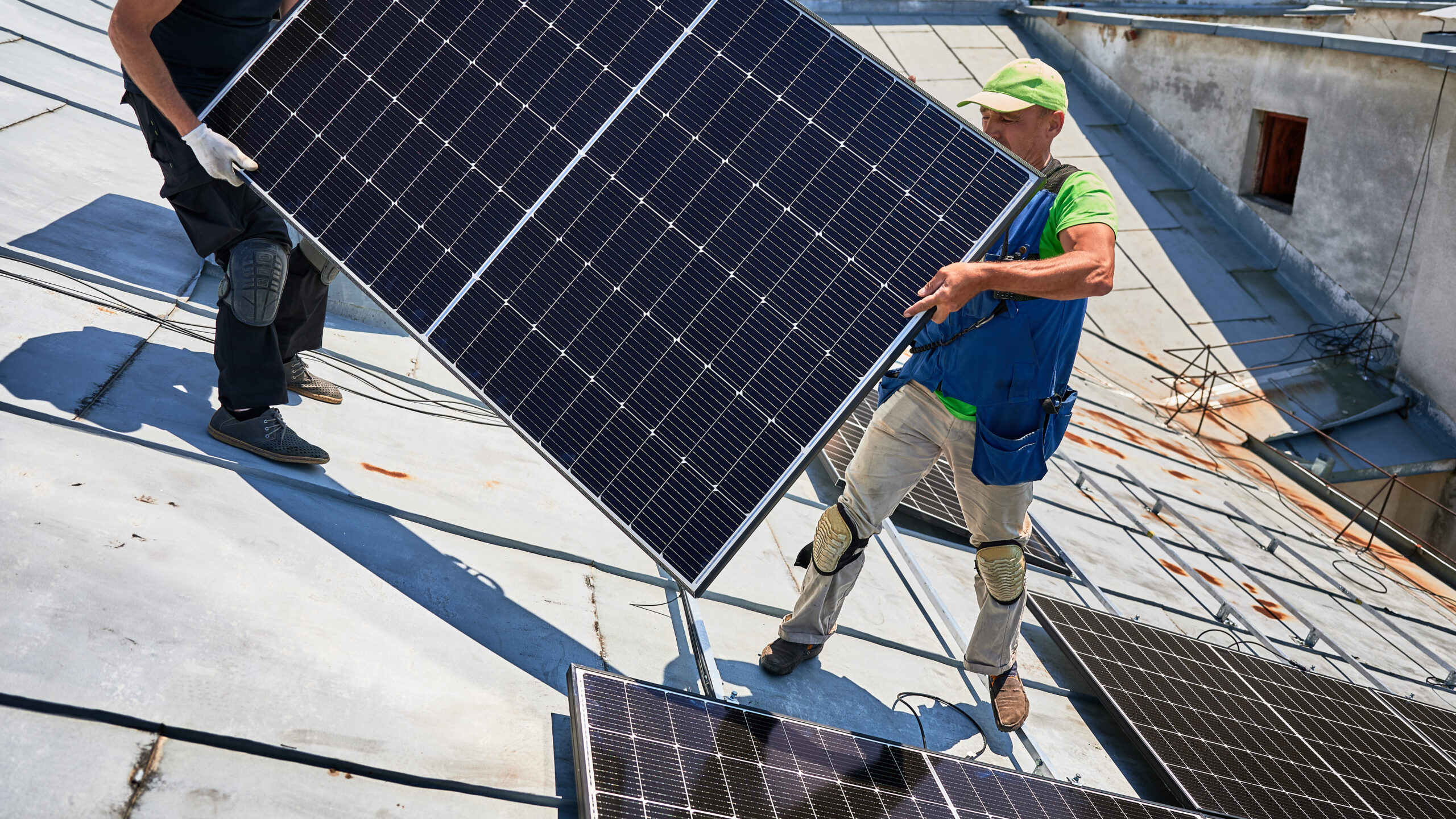 Workers building solar panel system on roof of house. Installers carrying photovoltaic solar module